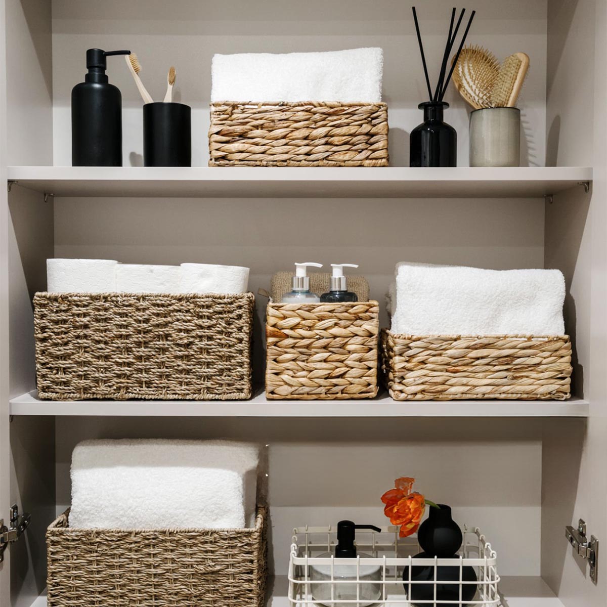 Household items, toilet paper rolls, white bath towels and cosmetics bottles on shelves in the bathroom cabinet.